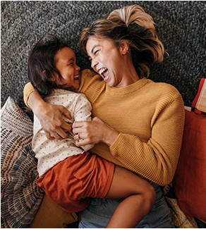 Happy mother and daughter lying on the floor in their play area.